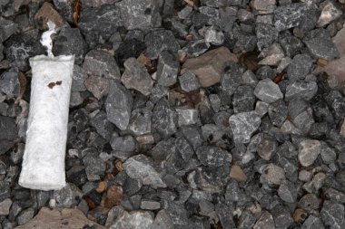 close up of gravel, stones, and sticks with a used old cigarette butt littered in it. Top view.