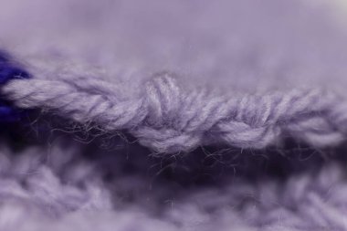 Eflatun mor bir battaniyenin kenarındaki dikişler, örgü örülmüş ya da örülmüş, size büyükannenin evini hatırlatıyor, sıcak ve samimi bir arka plan.