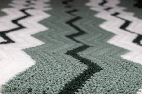 Büyükannemin eski zigzag çizgili battaniyesinin beyaz, koyu yeşil ve adaçayı yeşili, örülmüş ya da örülmüş, büyükannenin evi, rahat ve sıcak, dikey.