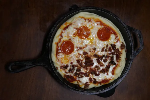 Yarısı biberli, yarısı pastırmalı küçük bir pizza. Koyu ahşap bir masaya yerleştirilmiş dökme demir bir tavada. Akşam yemeğinde pizza. İtalyan 00 unundan yapılmış.
