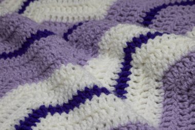 Büyükannemin retro zigzag çizgili battaniyesinin beyaz, eflatun, eflatun ve kraliyet moruyla örülmüş, örülmüş ya da örülmüş, büyükannesinin evi, rahat ve sıcak, dalgalı.