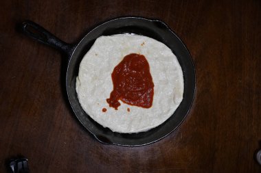 Bir kaşık dolusu soslu küçük pizza hamuru. Koyu ahşap bir masaya yerleştirilmiş dökme demir bir tavaya sıkıştırılmış. Akşam yemeğinde pizza. İtalyan 00 unundan yapılmış. Akşam yemeği için hazırlanıyorum..