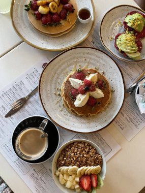 Restoran masasında kahvaltı tabakları, krepler, meyve ve kahve.