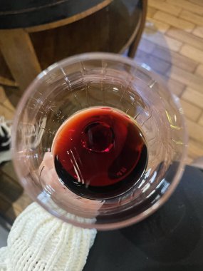 Arka planda ahşap bir masa olan kırmızı şarap kadehini tutan bir kadının el resmi, şarap mahzeni konsepti.