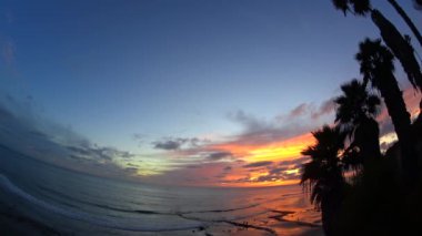 Swamis sahilinden gün batımı. Günbatımları, sörfçüler, siluetler, gelgit havuzları, palmiye ağaçları ve okyanus kaya heykelleri ile Güney Kaliforniya plaj sahneleri ve San Diego yakınlarındaki Swamis Resif Sörf Parkı, Ay ışığı ve Cardiff plajlarında Kaliforniya Encinitas.