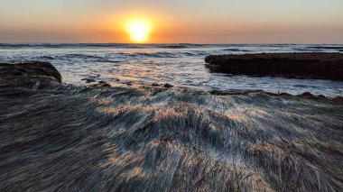 Negatif gelgit günbatımı sahnesi, eski bir resif yatağında büyüyen deniz çimlerini gösteriyor. Encinitas Ca 'daki Swamis Resif Sörf Parkı' nda gizli kumsallar, gün batımları, sörfçüler, gelgit havuzları, sahil kayalıkları, palmiye ağaçları ve şiddetli kış fırtınaları..