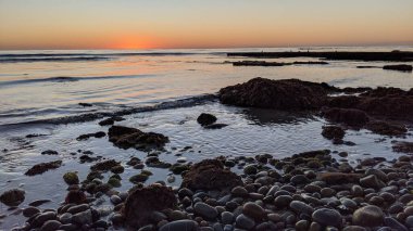 Günbatımları, sörfçüler, siluetler, gelgit havuzları, palmiye ağaçları ve okyanus kaya heykelleri ile Güney Kaliforniya plaj sahneleri Encinitas California 'da bulunan Swamis Resif Sörf Parkı' nda ABD Sahil Otoyolu 101..