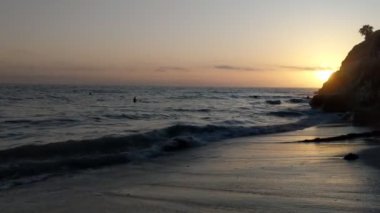 Pasifik Okyanusu 'nda gün batımı Swamis Point' te. Güney Kaliforniya sahilleri San Diego 'nun kuzeyinde. Sahil şeridi günbatımları, okyanus dalgaları, sörfçüler, gelgit havuzları, palmiye ağaçları ve Encinitas California 'daki Swamis Resif Sörf Parkı' ndaki kaya soyutlamaları..