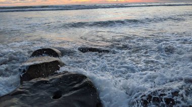 Swamis Sahili 'nin soğuk erimiş kayaları. 50 yıl önce kıyı şeridi boyunca uzanan okyanus dalgası erozyon kontrol taşları şimdi Swamis Resif Sörf Parkı Encinitas California 'daki antik nehir kayalarıyla çevrili soyut heykellere benziyor..