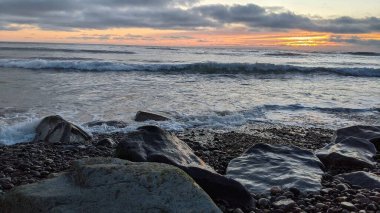 Swamis Sahili 'ndeki Nehir Kayalarının Serin Renkli Karışımı. Antik çağlarda hızla yuvarlanıp parlayan bu yuvarlak kayalar Swamis Resif Sörf Parkı Encinitas California 'daki erimiş kayaların heykelini yaptı..