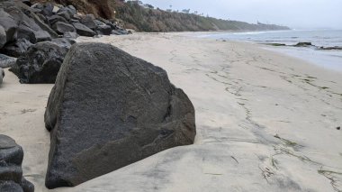 Swamis Sahili 'nin Erimiş Kayalıkları. 50 yıl önce kıyı boyunca uzanan erozyon kontrol kayaları Swamis Resif Sörf Parkı Encinitas California 'daki dalga enerjili kaya parlatıcı ekibindeki çok renkli nehir kayalarıyla çevrili..