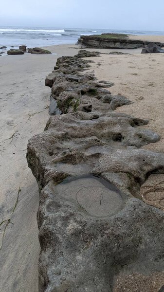 Искусство расплавленных скал пляжа Свами. Эрозионно-контрольные валуны, положенные вдоль берега 50 лет назад, теперь окружены древними разноцветными речными породами, все на волновой полировке скал в Swamis Reef Surf Park Encinitas California.