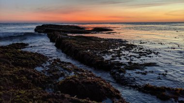 Güney Kaliforniya 'da, San Diego' nun kuzeyinde dalgalar alçak. Sahil şeridi günbatımları, okyanus dalgaları, sörfçüler, gelgit havuzları, palmiye ağaçları ve Encinitas California 'daki Swamis Resif Sörf Parkı' ndaki kaya soyutlamaları..