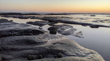 San Diego 'nun kuzeyinde Güney Kaliforniya sahilleri - Encinitas Kaliforniya' daki Swamis Resif Sörf Parkı 'nda günbatımı, sörfçüler, gelgit havuzları, dalgalar, kayalar, kum ve palmiye ağaçları.