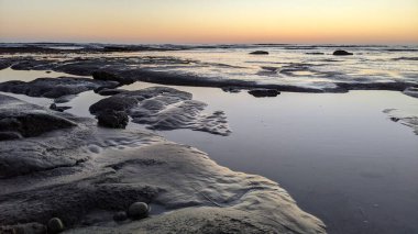 San Diego 'nun kuzeyinde Güney Kaliforniya sahilleri - Encinitas Kaliforniya' daki Swamis Resif Sörf Parkı 'nda günbatımı, sörfçüler, gelgit havuzları, dalgalar, kayalar, kum ve palmiye ağaçları.