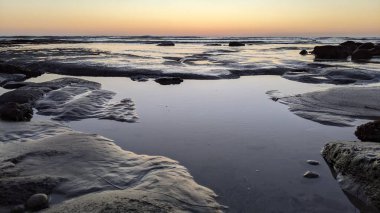 San Diego 'nun kuzeyinde Güney Kaliforniya sahilleri - Encinitas Kaliforniya' daki Swamis Resif Sörf Parkı 'nda günbatımı, sörfçüler, gelgit havuzları, dalgalar, kayalar, kum ve palmiye ağaçları.