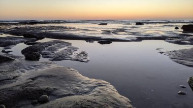 San Diego 'nun kuzeyinde Güney Kaliforniya sahilleri - Encinitas Kaliforniya' daki Swamis Resif Sörf Parkı 'nda günbatımı, sörfçüler, gelgit havuzları, dalgalar, kayalar, kum ve palmiye ağaçları.