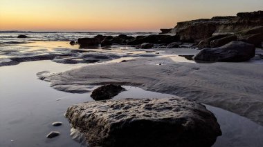 San Diego 'nun kuzeyinde Güney Kaliforniya sahilleri - Encinitas Kaliforniya' daki Swamis Resif Sörf Parkı 'nda günbatımı, sörfçüler, gelgit havuzları, dalgalar, kayalar, kum ve palmiye ağaçları.