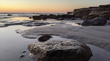 San Diego 'nun kuzeyinde Güney Kaliforniya sahilleri - Encinitas Kaliforniya' daki Swamis Resif Sörf Parkı 'nda günbatımı, sörfçüler, gelgit havuzları, dalgalar, kayalar, kum ve palmiye ağaçları.