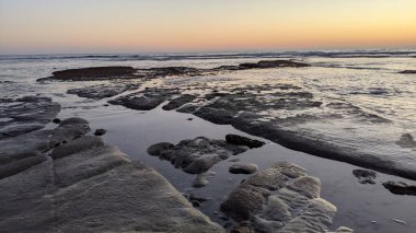 San Diego 'nun kuzeyinde Güney Kaliforniya sahilleri - Encinitas Kaliforniya' daki Swamis Resif Sörf Parkı 'nda günbatımı, sörfçüler, gelgit havuzları, dalgalar, kayalar, kum ve palmiye ağaçları.