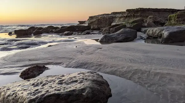 San Diego 'nun kuzeyinde Güney Kaliforniya sahilleri - Encinitas Kaliforniya' daki Swamis Resif Sörf Parkı 'nda günbatımı, sörfçüler, gelgit havuzları, dalgalar, kayalar, kum ve palmiye ağaçları.
