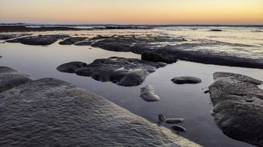 San Diego 'nun kuzeyinde Güney Kaliforniya sahilleri - Encinitas Kaliforniya' daki Swamis Resif Sörf Parkı 'nda günbatımı, sörfçüler, gelgit havuzları, dalgalar, kayalar, kum ve palmiye ağaçları.