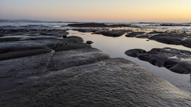 San Diego 'nun kuzeyinde Güney Kaliforniya sahilleri - Encinitas Kaliforniya' daki Swamis Resif Sörf Parkı 'nda günbatımı, sörfçüler, gelgit havuzları, dalgalar, kayalar, kum ve palmiye ağaçları.
