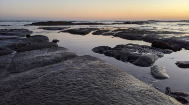 San Diego 'nun kuzeyinde Güney Kaliforniya sahilleri - Encinitas Kaliforniya' daki Swamis Resif Sörf Parkı 'nda günbatımı, sörfçüler, gelgit havuzları, dalgalar, kayalar, kum ve palmiye ağaçları.