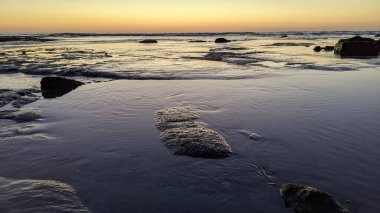 San Diego 'nun kuzeyinde Güney Kaliforniya sahilleri - Encinitas Kaliforniya' daki Swamis Resif Sörf Parkı 'nda günbatımı, sörfçüler, gelgit havuzları, dalgalar, kayalar, kum ve palmiye ağaçları.
