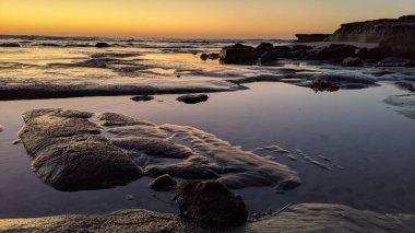 San Diego 'nun kuzeyinde Güney Kaliforniya sahilleri - Encinitas Kaliforniya' daki Swamis Resif Sörf Parkı 'nda günbatımı, sörfçüler, gelgit havuzları, dalgalar, kayalar, kum ve palmiye ağaçları.