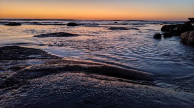 San Diego 'nun kuzeyinde Güney Kaliforniya sahilleri - Encinitas Kaliforniya' daki Swamis Resif Sörf Parkı 'nda günbatımı, sörfçüler, gelgit havuzları, dalgalar, kayalar, kum ve palmiye ağaçları.