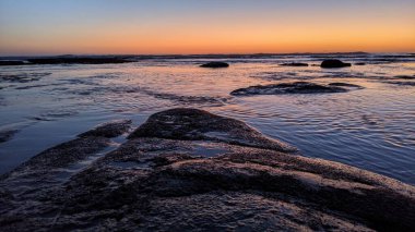 San Diego 'nun kuzeyinde Güney Kaliforniya sahilleri - Encinitas Kaliforniya' daki Swamis Resif Sörf Parkı 'nda günbatımı, sörfçüler, gelgit havuzları, dalgalar, kayalar, kum ve palmiye ağaçları.