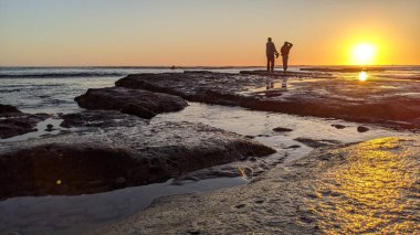 Günbatımları, sörfçüler, gelgit havuzları, palmiye ağaçları ve Swamis Resif Parkı Encinitas California sahilindeki doğal yontulmuş plaj kayaları olan Güney Kaliforniya sahili manzarası..
