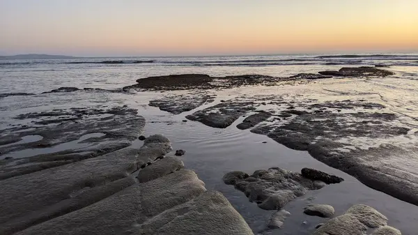 San Diego 'nun kuzeyinde Güney Kaliforniya sahilleri - Encinitas Kaliforniya' daki Swamis Resif Sörf Parkı 'nda günbatımı, sörfçüler, gelgit havuzları, dalgalar, kayalar, kum ve palmiye ağaçları.