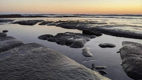 San Diego 'nun kuzeyinde Güney Kaliforniya sahilleri - Encinitas Kaliforniya' daki Swamis Resif Sörf Parkı 'nda günbatımı, sörfçüler, gelgit havuzları, dalgalar, kayalar, kum ve palmiye ağaçları.