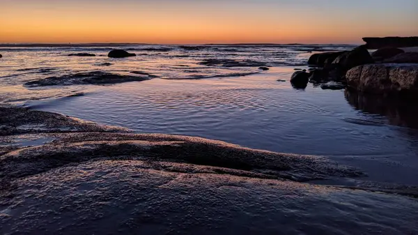 San Diego 'nun kuzeyinde Güney Kaliforniya sahilleri - Encinitas Kaliforniya' daki Swamis Resif Sörf Parkı 'nda günbatımı, sörfçüler, gelgit havuzları, dalgalar, kayalar, kum ve palmiye ağaçları.