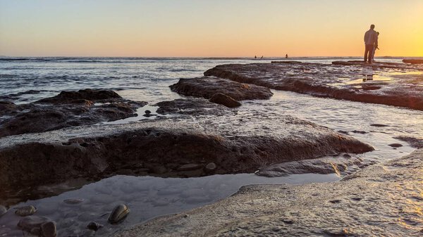 Южная Калифорния пляжные пейзажи с закатами, серферы, бассейны приливов, пальмы и природные скульптурные пляжные скалы на берегу в Swamis Reef Surf Park Encinitas Калифорния.