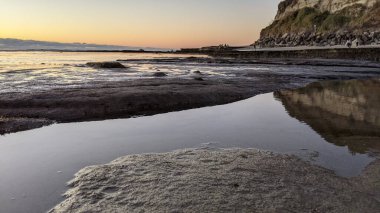 Swamis Resif Parkı Encinitas 'ta gelgit havuzları, okyanus dalgaları ve alacakaranlık renkli gökyüzü olan antik bir resifte günbatımı sörf sahnesi..