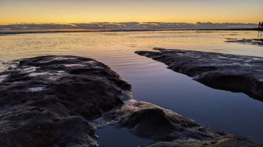 Swamis Resif Parkı Encinitas 'ta gelgit havuzları, okyanus dalgaları ve alacakaranlık renkli gökyüzü olan antik bir resifte günbatımı sörf sahnesi..