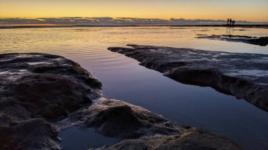 Swamis Resif Parkı Encinitas 'ta gelgit havuzları, okyanus dalgaları ve alacakaranlık renkli gökyüzü olan antik bir resifte günbatımı sörf sahnesi..
