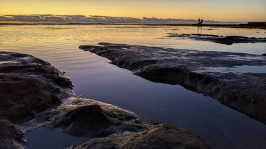 Swamis Resif Parkı Encinitas 'ta gelgit havuzları, okyanus dalgaları ve alacakaranlık renkli gökyüzü olan antik bir resifte günbatımı sörf sahnesi..