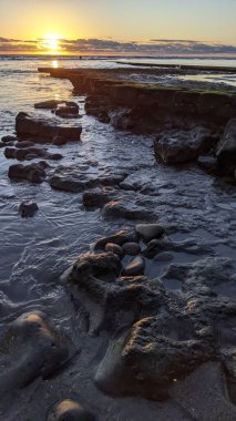 Swamis Resif Parkı Encinitas 'ta gelgit havuzları, okyanus dalgaları ve alacakaranlık renkli gökyüzü olan antik bir resifte günbatımı sörf sahnesi..
