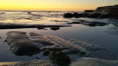 San Diego yakınlarındaki Güney Kaliforniya plaj sahneleri - Encinitas California 'daki Swamis Resif Sörf Parkı' nda günbatımı, sörfçüler, gelgit havuzları, dalgalar, kayalar, kum ve palmiye ağaçları.