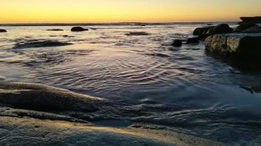 San Diego yakınlarındaki Güney Kaliforniya plaj sahneleri - Encinitas California 'daki Swamis Resif Sörf Parkı' nda günbatımı, sörfçüler, gelgit havuzları, dalgalar, kayalar, kum ve palmiye ağaçları.