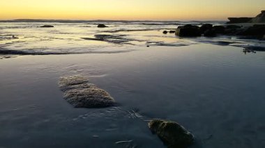 San Diego yakınlarındaki Güney Kaliforniya plaj sahneleri - Encinitas California 'daki Swamis Resif Sörf Parkı' nda günbatımı, sörfçüler, gelgit havuzları, dalgalar, kayalar, kum ve palmiye ağaçları.