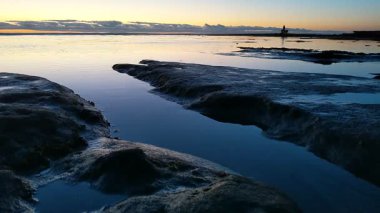 San Diego yakınlarındaki Güney Kaliforniya plaj sahneleri - Encinitas California 'daki Swamis Resif Sörf Parkı' nda günbatımı, sörfçüler, gelgit havuzları, dalgalar, kayalar, kum ve palmiye ağaçları.