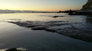 Güney Kaliforniya plaj manzarası - Encinitas California 'daki Swamis Resif Sörf Parkı' nda günbatımı, sörfçüler, gelgit havuzları, dalgalar, kayalar, kum ve palmiye ağaçları.