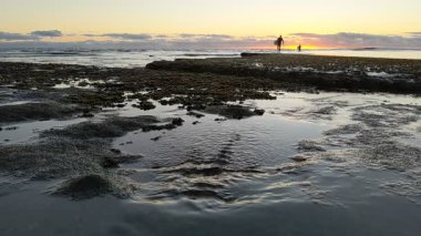 Güney Kaliforniya plaj manzarası - Encinitas California 'daki Swamis Resif Sörf Parkı' nda günbatımı, sörfçüler, gelgit havuzları, dalgalar, kayalar, kum ve palmiye ağaçları.
