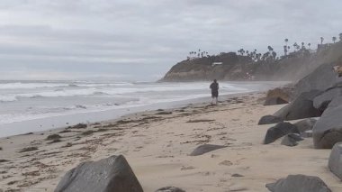 Güney Kaliforniya plaj manzarası - Encinitas California 'daki Swamis Resif Sörf Parkı' nda günbatımı, sörfçüler, gelgit havuzları, dalgalar, kayalar, kum ve palmiye ağaçları.