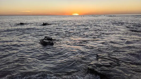 Sahilde yürüyen bir sörfçü. Güney Kaliforniya plajları, günbatımları, dalgalar, sörfçüler, gelgit havuzları, bulutlar ve palmiye ağaçları Encinitas California 'daki Swamis Resif Sörf Parkı' nda. San Diego 'nun 25 mil kuzeyinde yer alıyor..